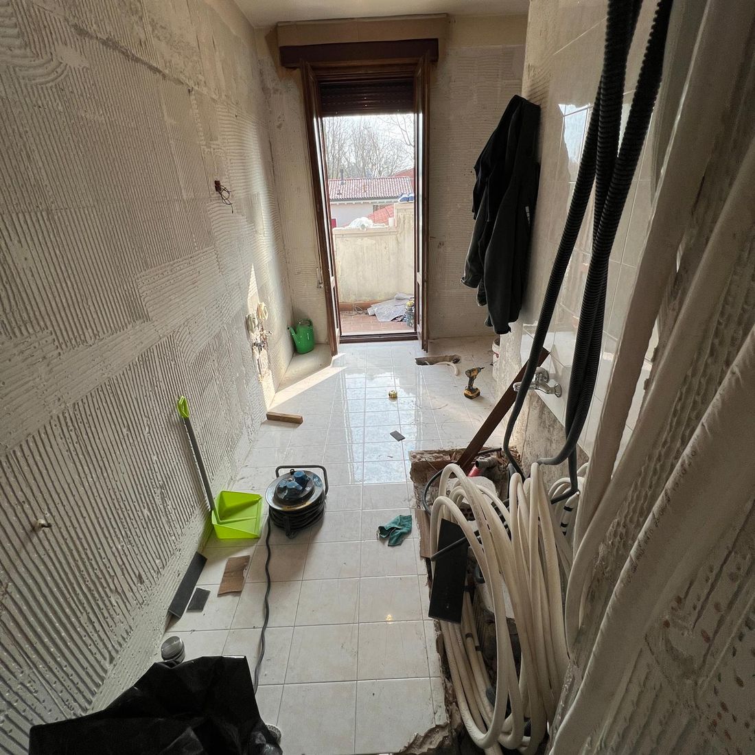 Bagno in fase di demolizione: pareti spogliate e impianti in vista, porta finestra sul fondo