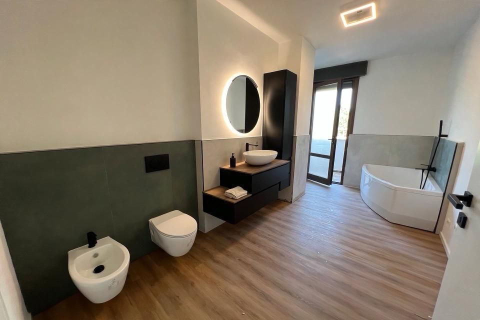 Lo stesso bagno finito: sanitari sospesi, mobile sospeso con specchio led, vasca angolare e pavimento in finto legno
